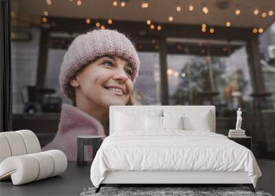 Fashionable mature woman in a pink knitted beanie hat and stylish coat outdoors in a cafe in autumn. Middle aged woman positive and smiling with pigtails in the city. Blur and selective focus Wall mural