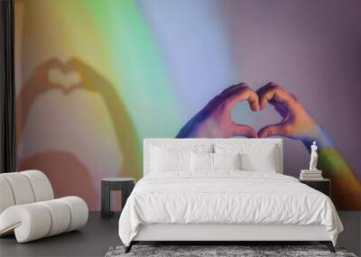 Gay pride concept. Handmade Heart Sign with Gay Pride LGBT. female hands show a heart-shaped figure folded from fingers on a rainbow background. Rainbow light from a prism Wall mural