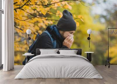 man sneezes and blows his nose in a handkerchief in an autumn park Wall mural