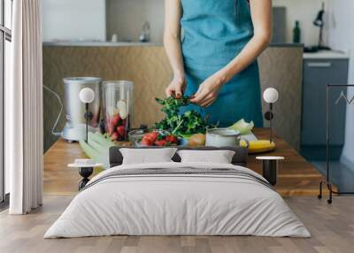 A female cook in a blue apron prepares a vegan fruit cocktail in her home kitchen. Healthy lifestyle and eating concept. Wall mural