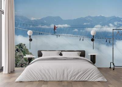 A person walks on a suspended rope bridge in the clouds. Extreme attraction. Wanderlust and adventures. Wall mural