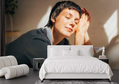 A woman lies on a bed in bright sunlight from the window. Wall mural