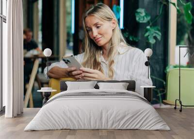 A woman uses a mobile phone to communicate while sitting in a coffee house. Wall mural