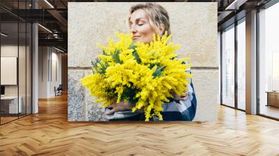 Close up portrait of attractive white woman holding fresh spring fresh bouquet of mimosa. Wall mural