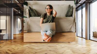 Happy smiling young woman working from home on laptop while sitting on the floor. Wall mural