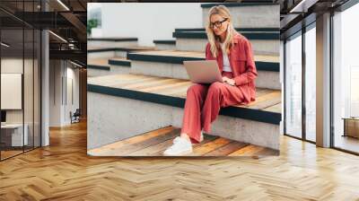 Modern millennial woman sitting in the park working on a laptop. Wall mural