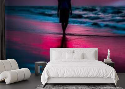 silhouette of a person walking on the beach at sunrise with red sky and blue sea.  Wall mural