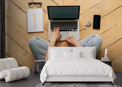 Top view of anonymous lady typing on keypad sitting on wooden floor with notebook and mobile Wall mural