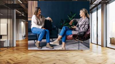 Two modern stylish women are sitting in the office discussing ideas and implementation of plans. A confidential conversation between a woman and a consultant psychologist. Wall mural