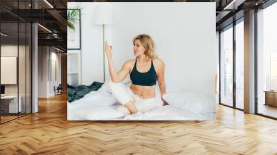 Woman in sportswear doing yoga in the morning while sitting in bed. Wall mural