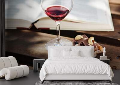 Glass with wine and pieces of chocolate near open book Wall mural