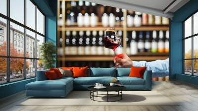 Person Holding Glass of Red Wine in Wine Store With Blurred Shelf Background Wall mural