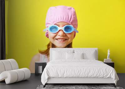 Smiling little girl in swimming cap and glasses on colored background. Wall mural