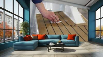 A man's hand rubs oil on marine teak on the deck of a white motor yacht , motor boat maintenance Wall mural