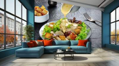 Chicken Caesar salad with the classic dressing being poured, croutons, and pepper, on a black background Wall mural