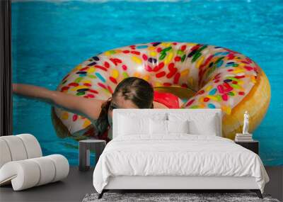 pretty young girl playing with her donut-shaped buoy in the swimming pool Wall mural