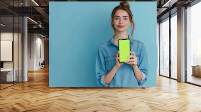 A woman is holding a green phone in front of a blue wall. The phone is turned off and the screen is blank Wall mural