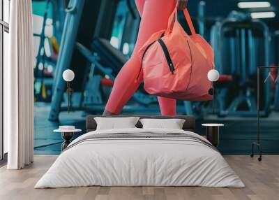 A woman wearing pink leggings and carrying a pink bag walks through a gym. The gym is filled with various pieces of equipment, including a bench, a chair, and a few treadmills Wall mural