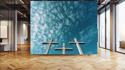 Three crosses are standing in a row on a cloudy day. The sky is blue and the clouds are white Wall mural