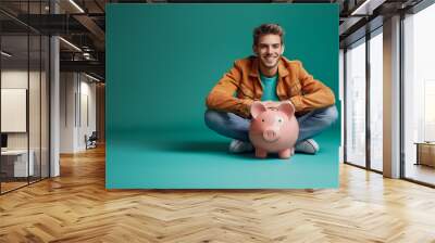 A cheerful man sitting with a piggy bank in front of a teal background, representing savings and financial planning.  Generative AI Wall mural