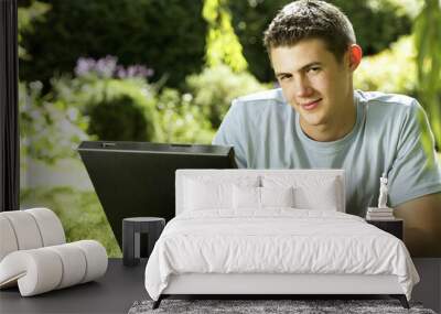 Teenage boy lying on the field using laptop Wall mural