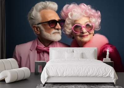 Stylish elderly couple in pink outfits and sunglasses against dark blue background. Wall mural