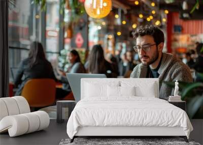 Digital nomad working from a laptop in a vibrant co-working space, with a diverse group of people in the background Wall mural