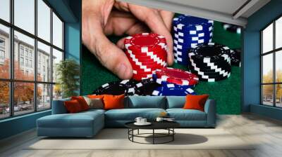 A Caucasian male hand placing a stack of red betting chips into the pot with other red, blue and black chips on a green felt gaming table surface.  Macro frame with high detail. Room for copy. Wall mural