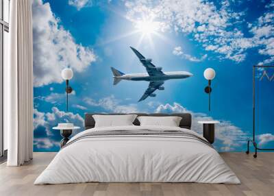 Airplane in the blue sky with clouds from below, high flying passenger plane. jet plane flying overhead diagonally in sky with sunlight. Bottom view Wall mural