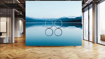 Serene landscape featuring reflective water and two circular objects, surrounded by majestic mountains and a clear blue sky. Wall mural