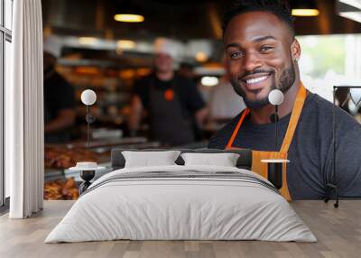 A cheerful chef wearing an orange apron stands in a barbecue restaurant, preparing delicious grilled meats for eager customers Wall mural