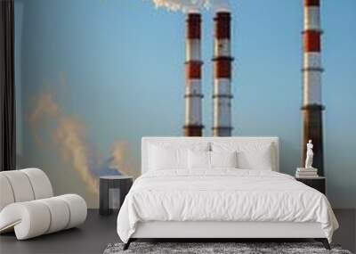 A large industrial plant with three tall red and orange smokestacks emitting smoke. The sky is clear and the sun is shining Wall mural