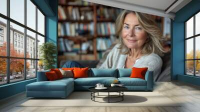 A woman is sitting on a couch in a room with a lot of books. She is smiling and looking at the camera Wall mural