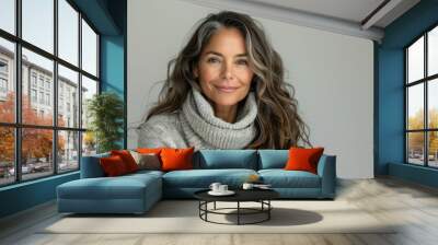 A woman with long, wavy, graying hair is wearing a grey sweater, smiling at the camera Wall mural