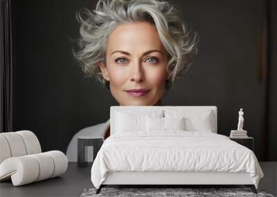 A woman with short, wavy, gray hair smiles softly at the camera. She is wearing a white button-down shirt. The background is a dark, neutral color Wall mural