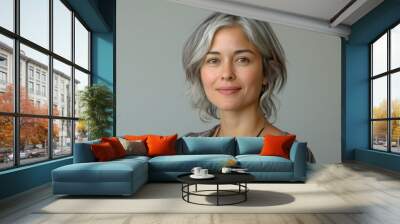 A woman with silver hair and a gentle smile looks directly at the camera against a muted gray backdrop. She wears a patterned blouse and a simple necklace Wall mural