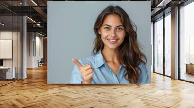 A young woman with long brown hair smiles while wearing a blue button-down shirt and pointing to the left with her right hand Wall mural