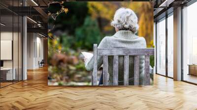 Elderly woman reading a book in the autumn garden. Wall mural