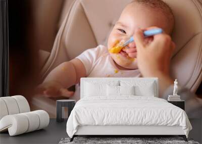 Happy baby eating porridge and smiling in high chair Wall mural