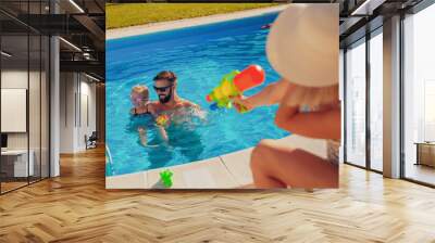 Parents and child playing with squirt guns at the swimming pool Wall mural