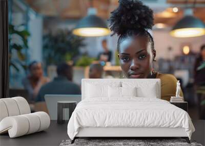 Attractive african young confident businesswoman sitting at the office table with group of colleagues in the background, working on laptop computer - generative ai Wall mural