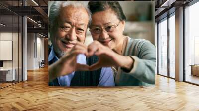 happy loving senior asian couple forming a heart shape with hand while video chatting with friends and family Wall mural