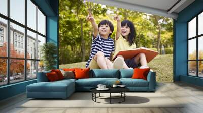 two beautiful asian children sitting on grass pointing to sky Wall mural