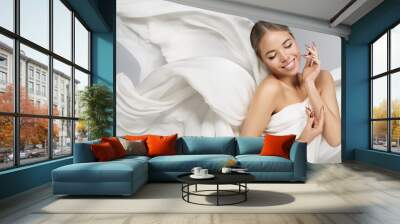 Beautiful Girl in White Silk flying Fabrics. Cheerful smiling Model Portrait over Gray. Happy Woman Face and Body Skin Care. Satin Cloth floating on Wind Wall mural