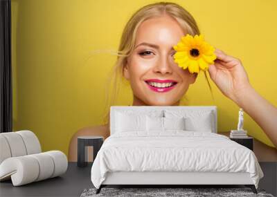 Happy Young Woman holding Yellow Flower in front of Eye. Cheerful Beauty Model Face over Orange background. Women Natural Facial and Body Skin Care Cosmetics. Smiling Summer Fashion Girl Wall mural