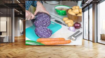 Men's hands cut red cabbage with a knife to make a salad on the kitchen table. Wall mural