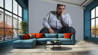 Overweight man sitting on chair in sad mood with chin resting on hand Wall mural