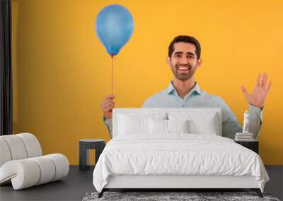 Portrait of happy young man holding balloon in hand and gesturing with palm Wall mural