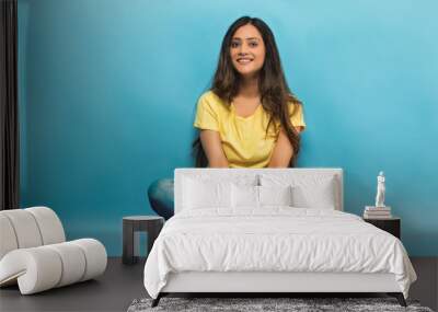 Smiling teenage girl in jeans and t-shirt sitting cross legged on the floor holding her leg
 Wall mural