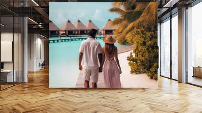 A man and woman couple in love hold hands and walk along the beach shore of an exotic blue water resort. View from back, vertical format. Creative concept of tropical beach vacation for newlyweds. Wall mural